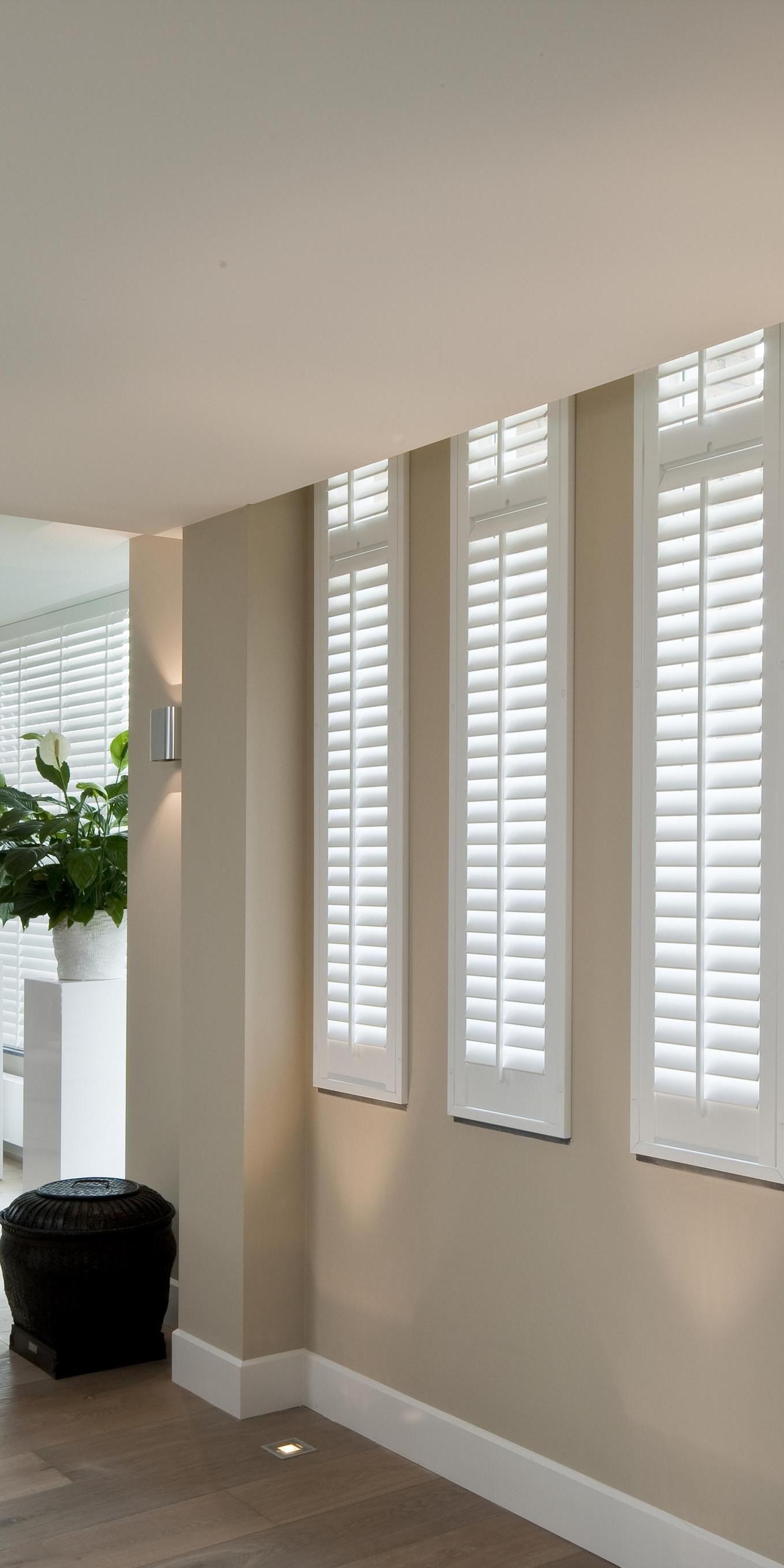 Helles Wohnzimmer mit großen weißen Fensterläden und moderner Einrichtung.