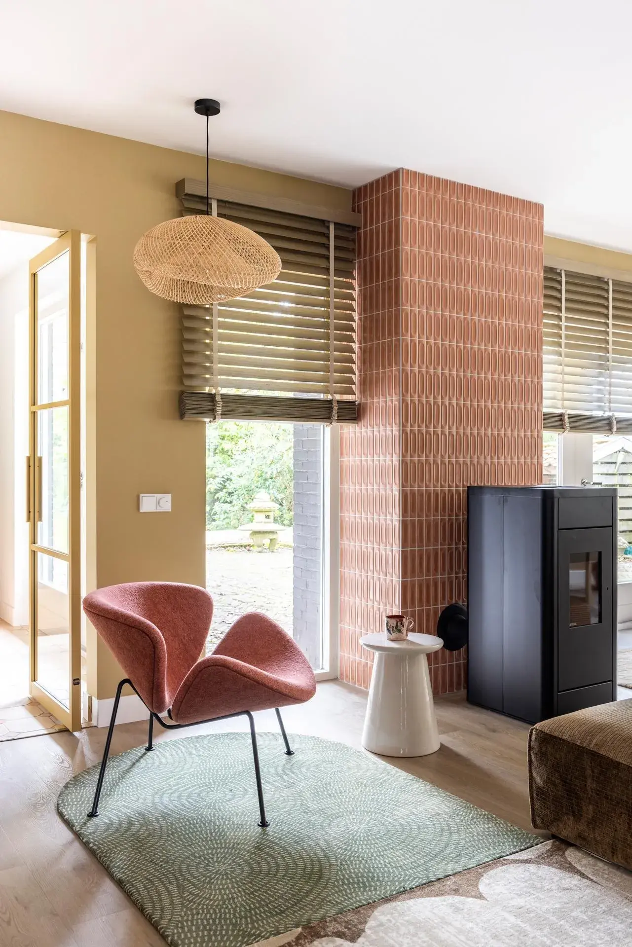 Modernes Wohnzimmer mit rosa Sessel, grünem Teppich und Holzjalousien.