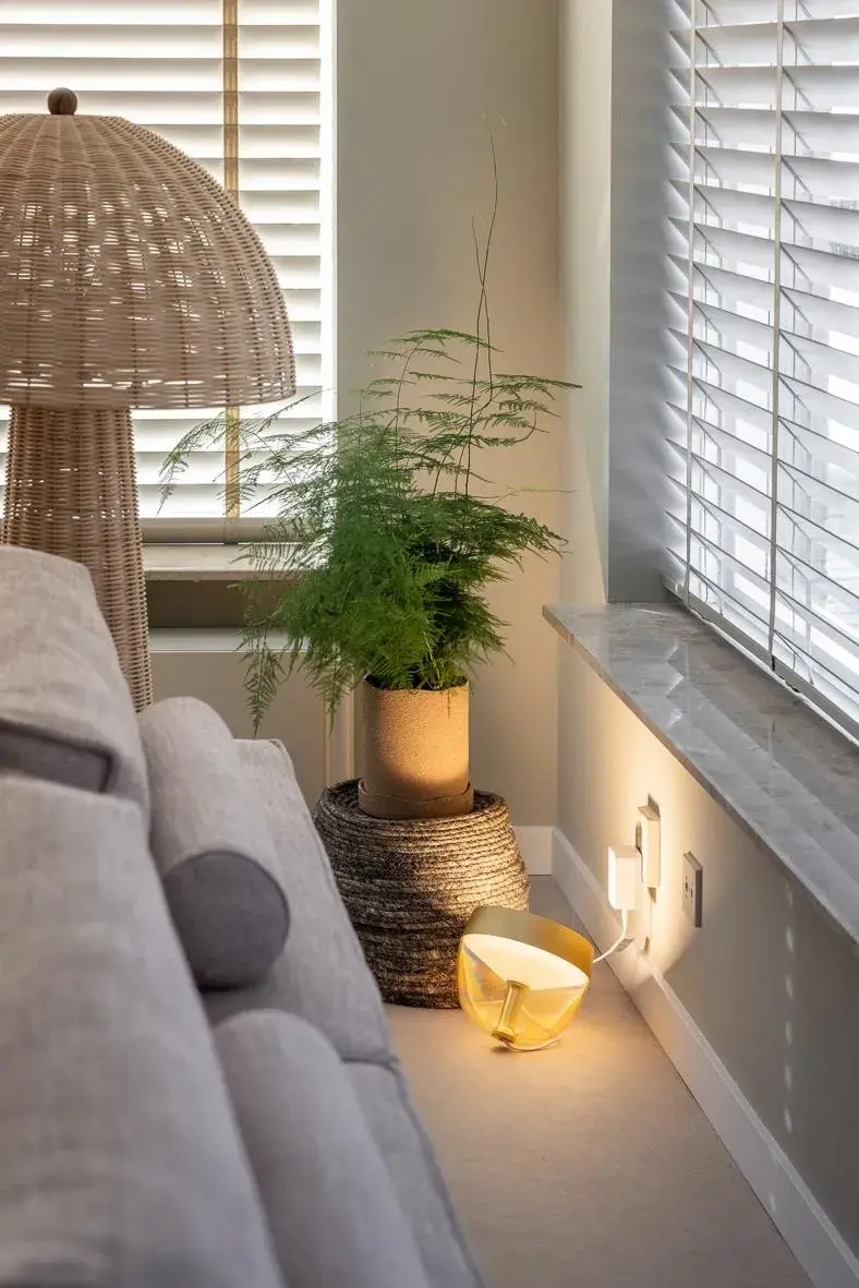 Helles Wohnzimmer mit Sofa, Pflanze, Stehlampe und gelber Lampe am Fenster.