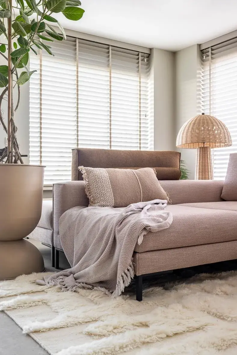 Helles Wohnzimmer mit beigem Sofa, Decke, Kissen, großem Blumentopf und Stehleuchte.