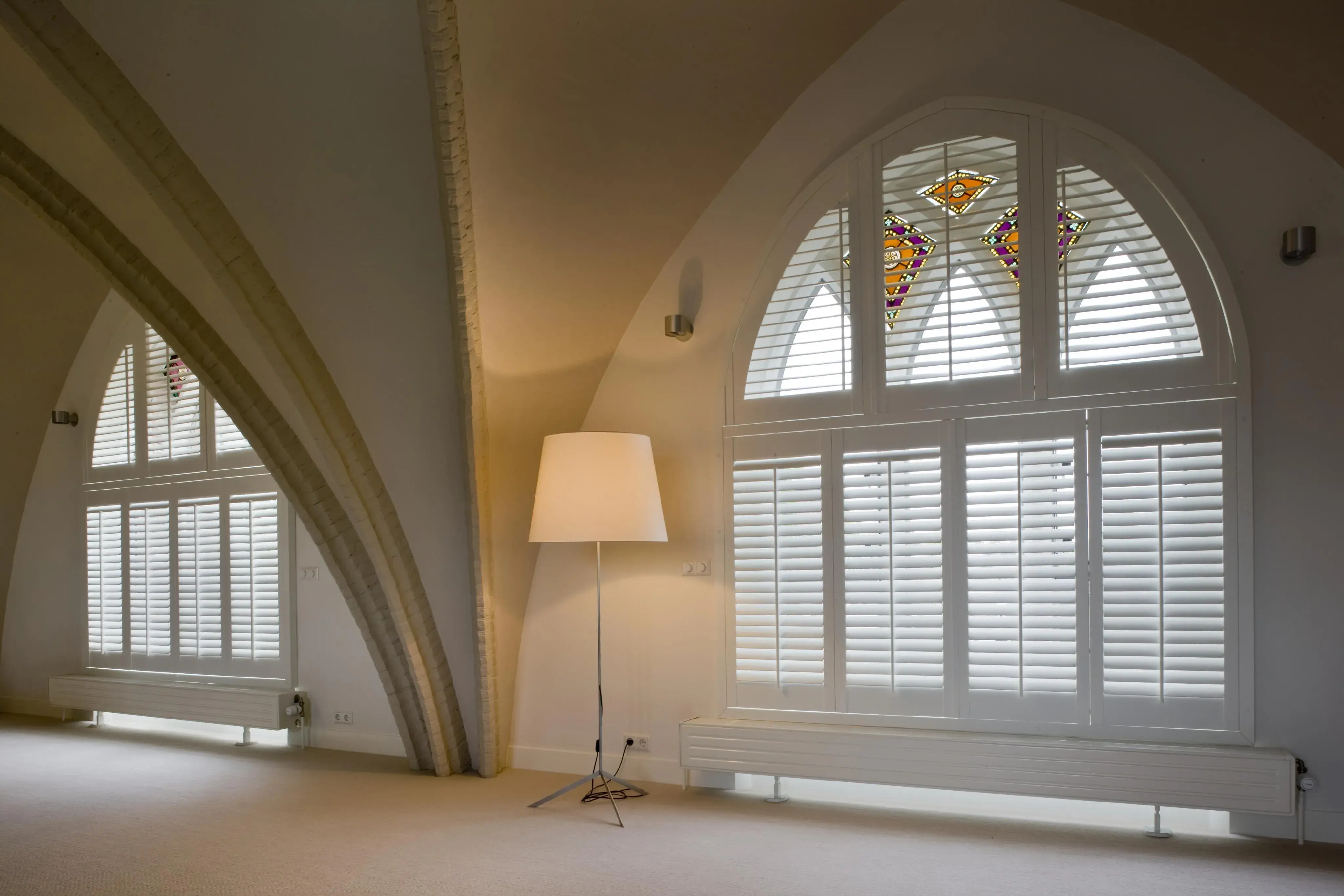 Helles Loft mit großen gotischen Fenstern und Stehlampe.
