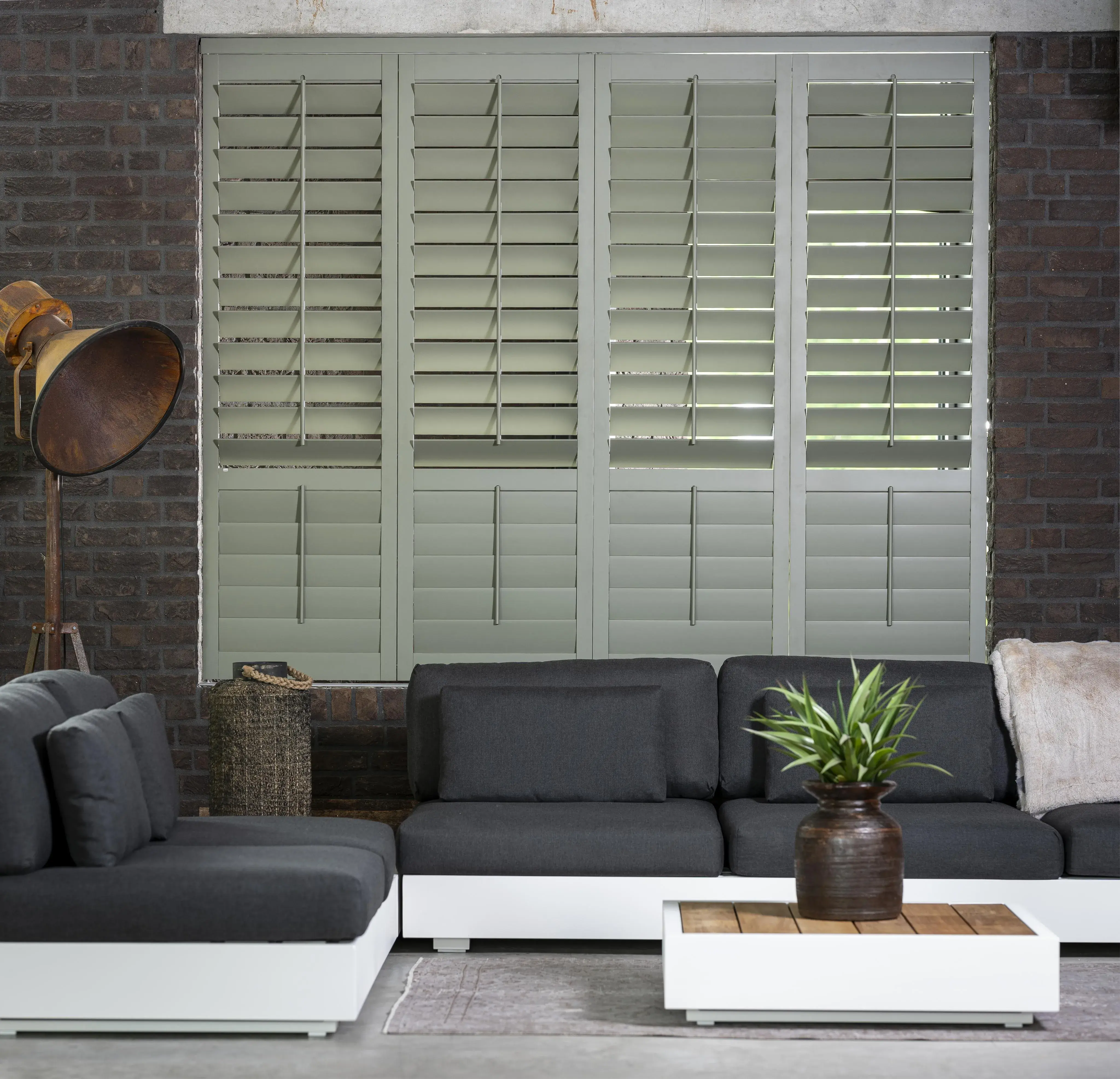 Modernes Wohnzimmer mit dunklen Sofas, weißen Tischen und großen Fensterläden