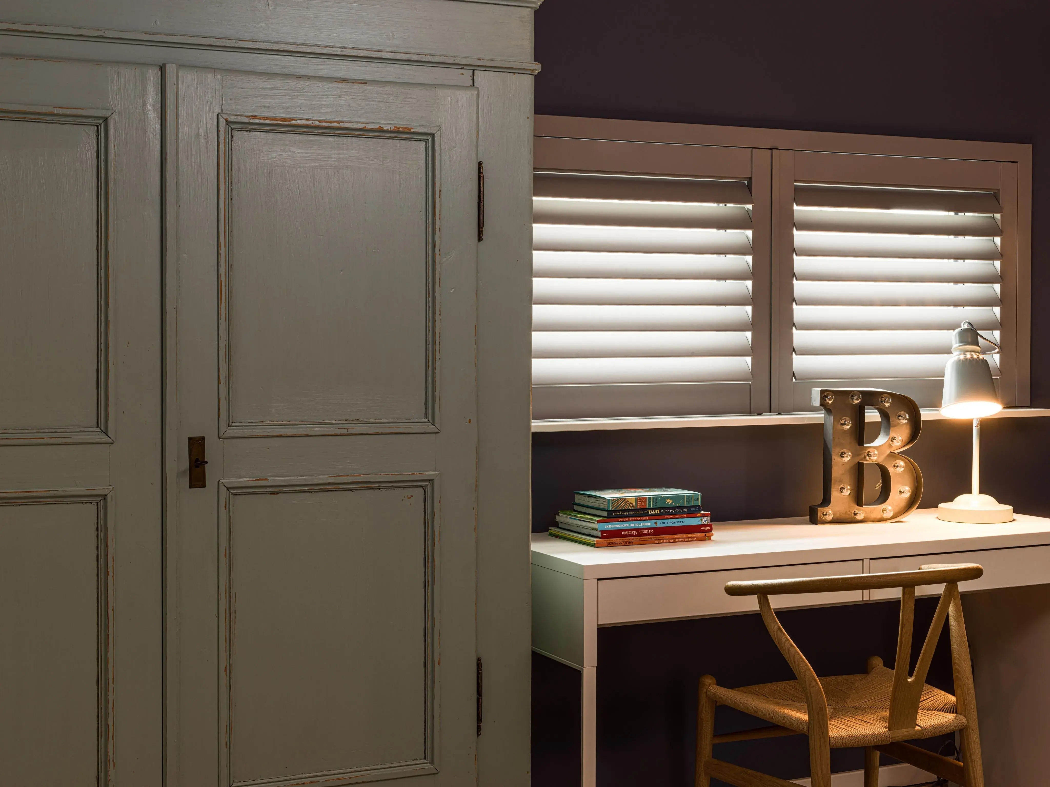 Holzschrank neben Schreibtisch mit Lampe, Stuhl, Büchern und goldfarbenem Buchstaben B.
